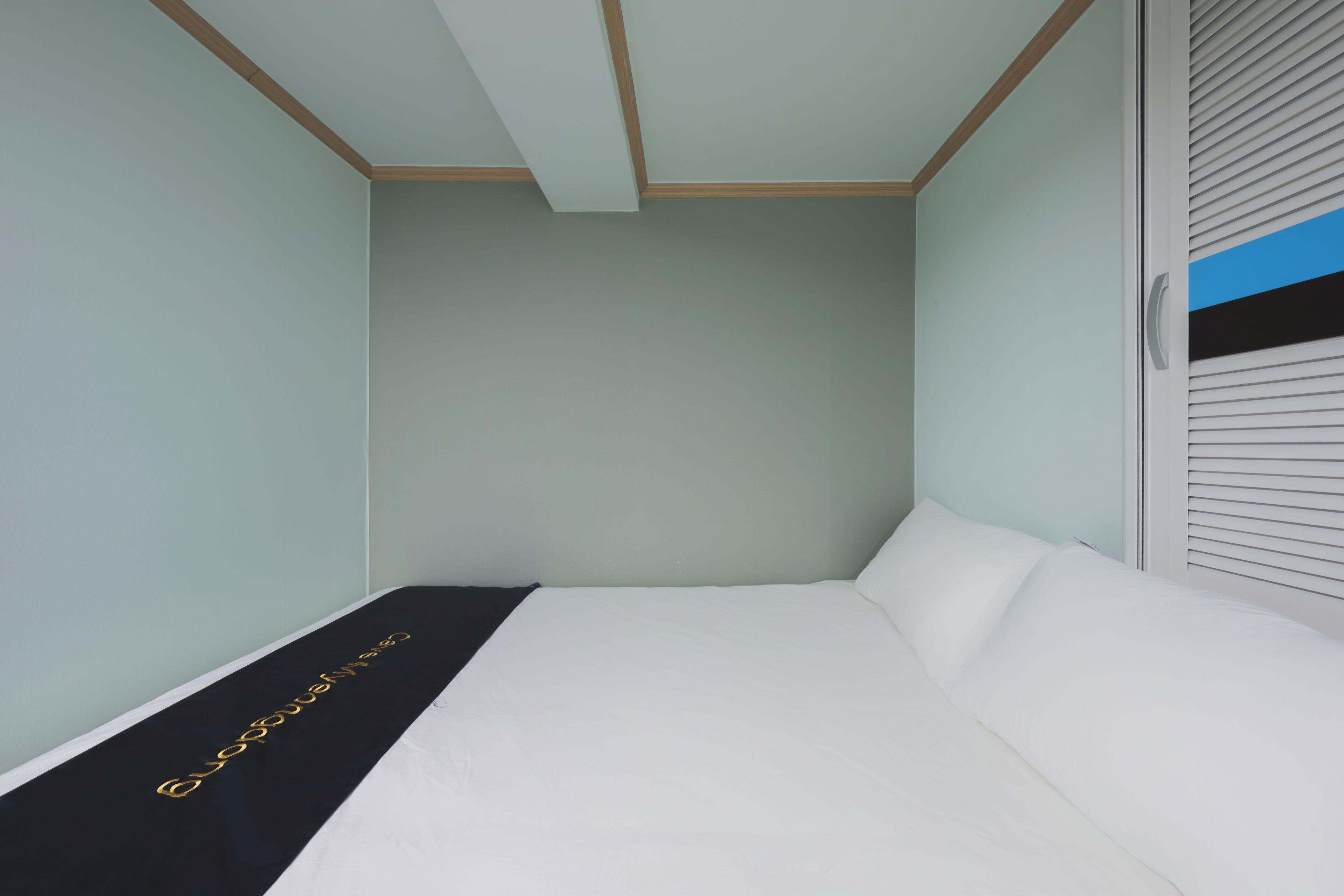 A bedroom with a bed, a black runner with gold lettering, and a window with blinds.