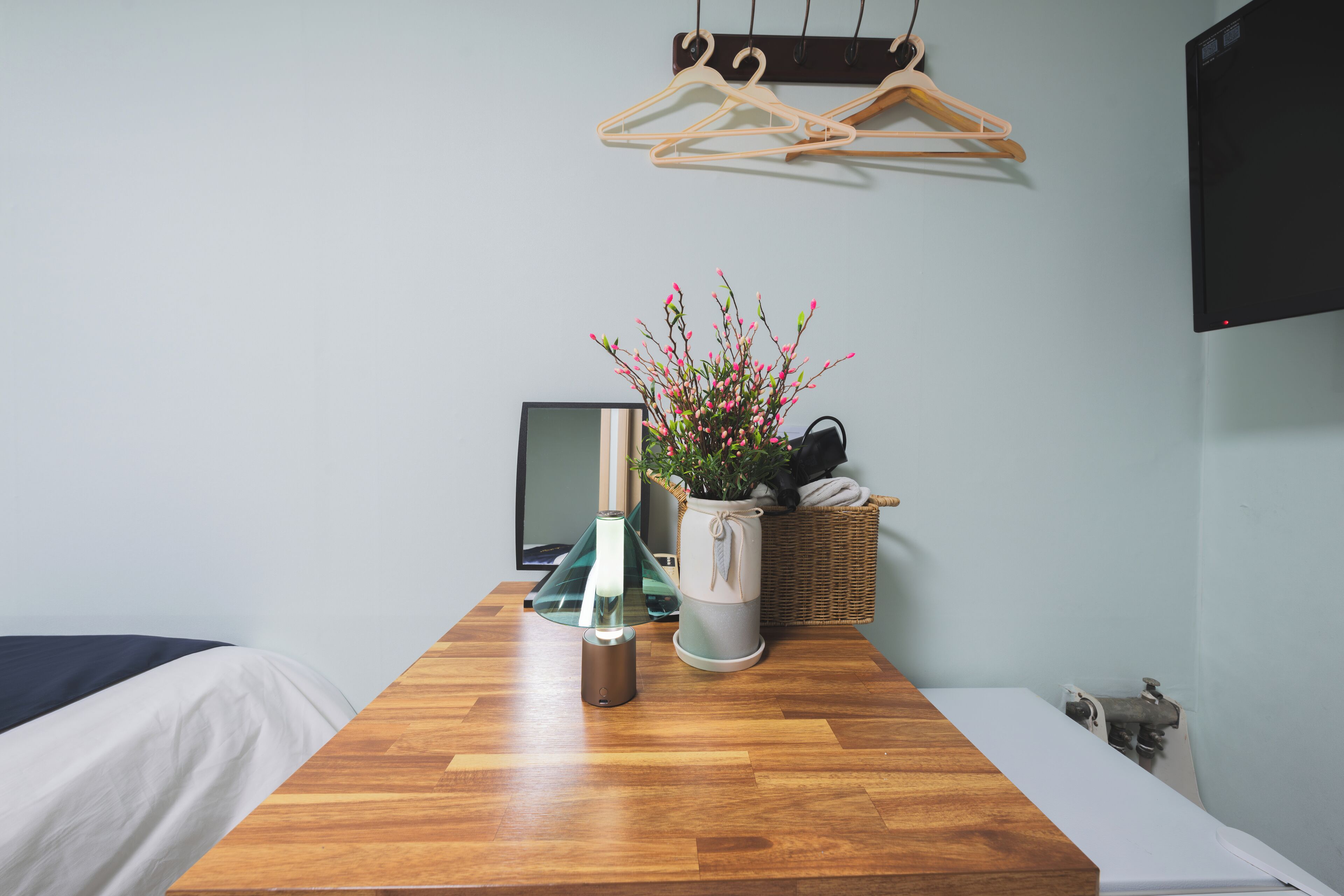 A room with a wooden table, a potted plant, a basket, and a hanging clothes rack.