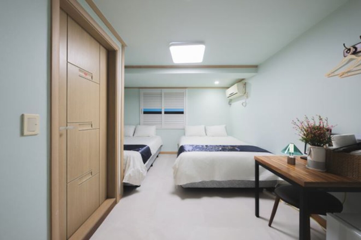 Un dormitorio con dos camas, un escritorio, una silla, una ventana con persianas, una lámpara de techo y un armario.