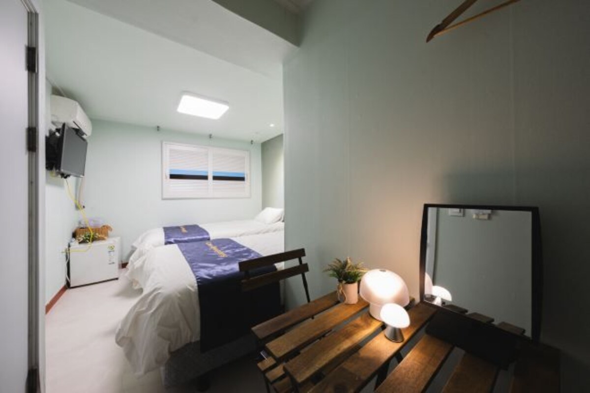 Un dormitorio con cama, mesita de noche, lámpara, espejo y ventana con persianas.