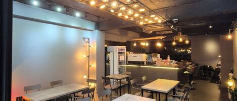 A modern cafe interior with multiple tables and chairs, a bar area, and pendant lighting.