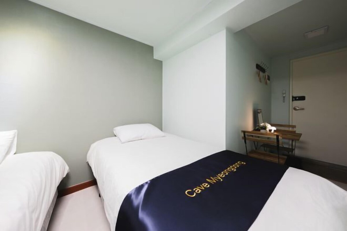 Quarto de hotel com duas camas, uma escrivaninha e uma porta.