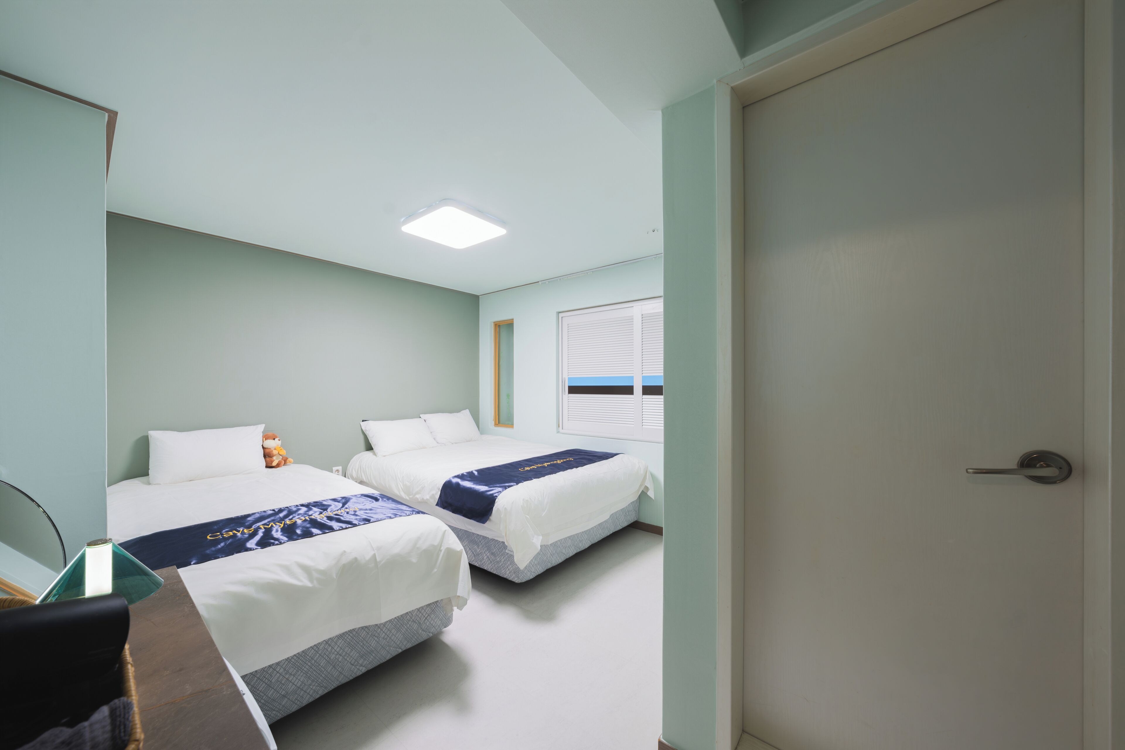 A hotel room with two beds, a desk, and a door.