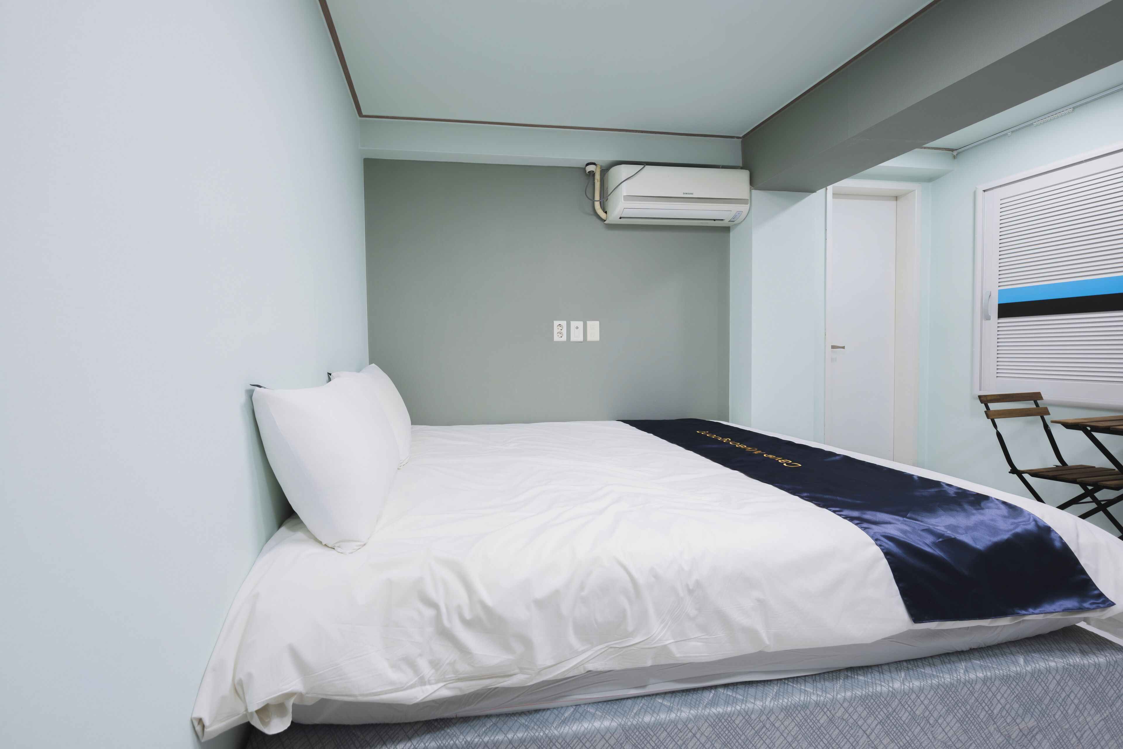 Una cama bien hecha con una colcha blanca y azul, una almohada blanca y un aire acondicionado de pared.