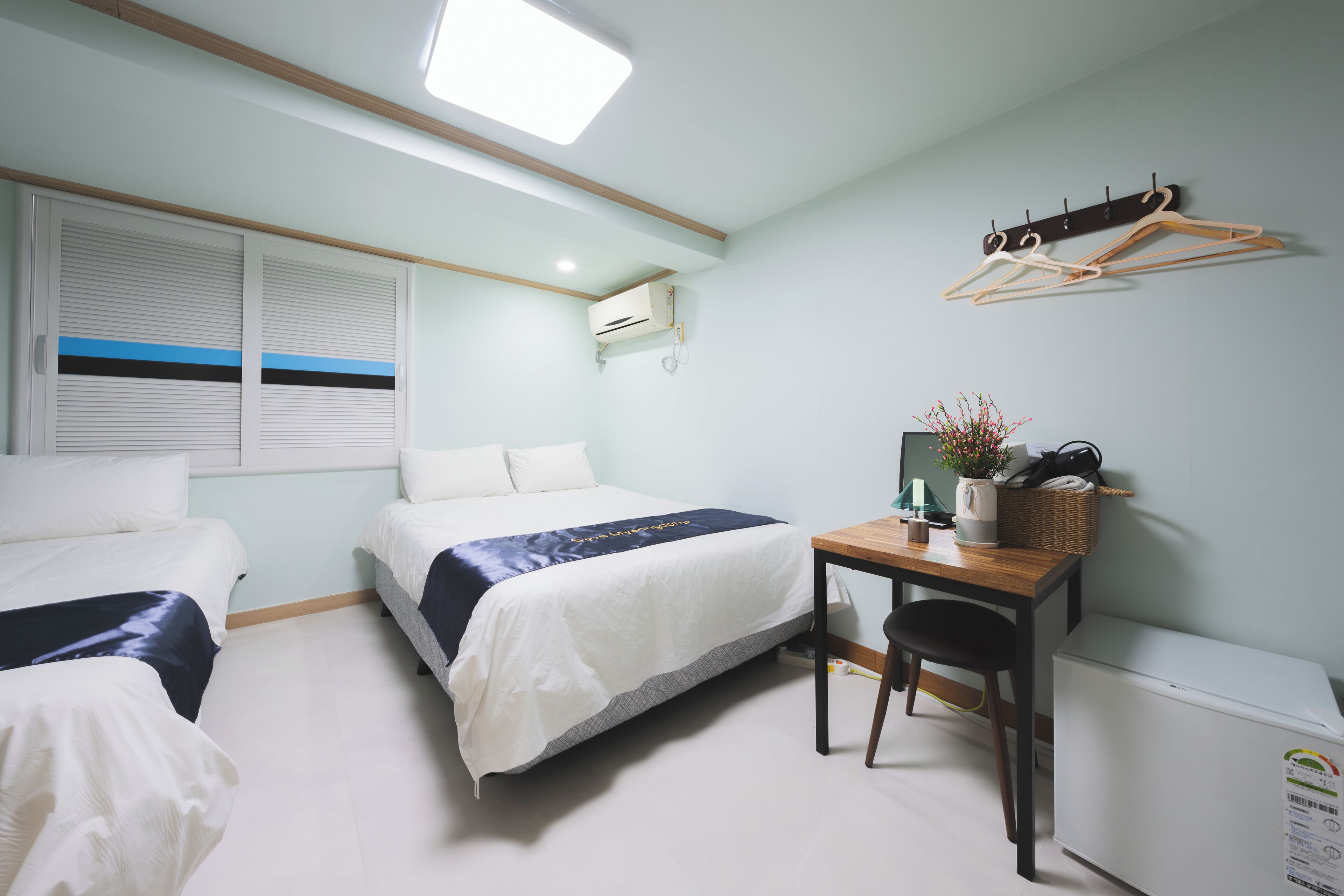 Ein Hotelzimmer mit zwei Betten, einem Schreibtisch, einem Stuhl, einem Heizkörper und einem Kleiderständer.