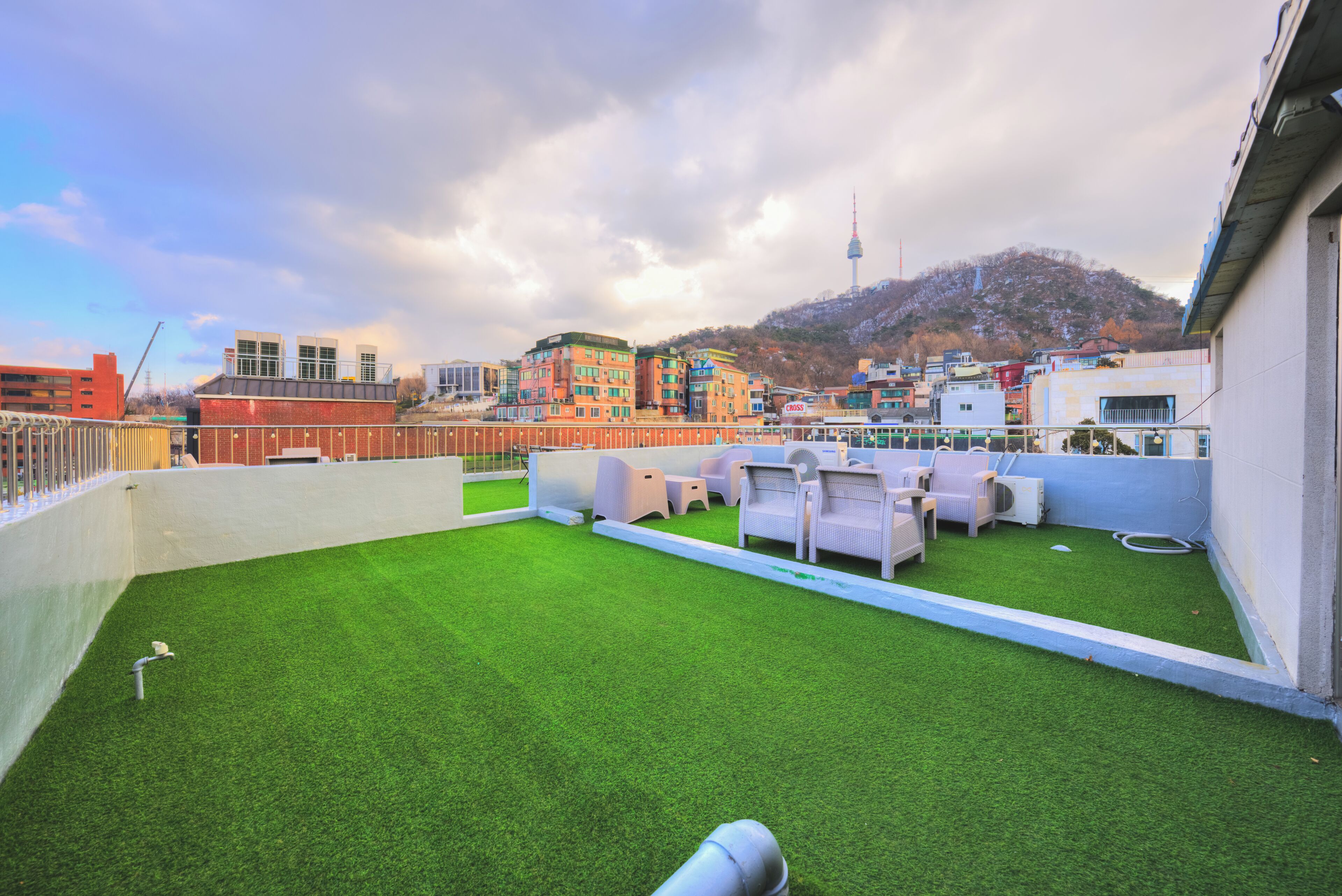 A rooftop terrace with artificial grass, white outdoor furniture, and a view of a cityscape including a tower.