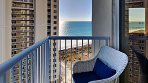 Un balcon avec un fauteuil en osier et une vue sur la plage et l’océan.