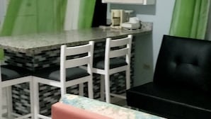 Een kleine, praktische kamer met een kitchenette, een eethoek met een tafel en stoelen, en een bank.