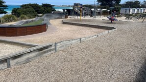 Un parque infantil con zona de juegos de arena y rampa de madera, con vistas a la playa.