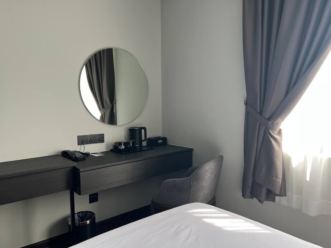 A hotel room with a bed, a desk with a telephone, a coffee maker, and a mirror.