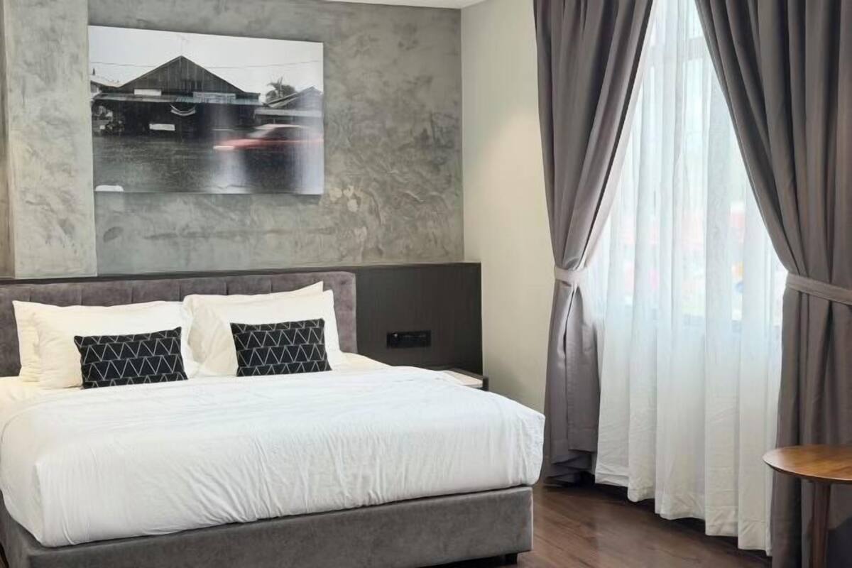 A modern bedroom with a large bed, a headboard, a wall-mounted picture, and a window with curtains.