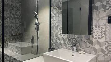 Un baño moderno con cabina de ducha de vidrio, un espejo grande y un lavabo blanco.