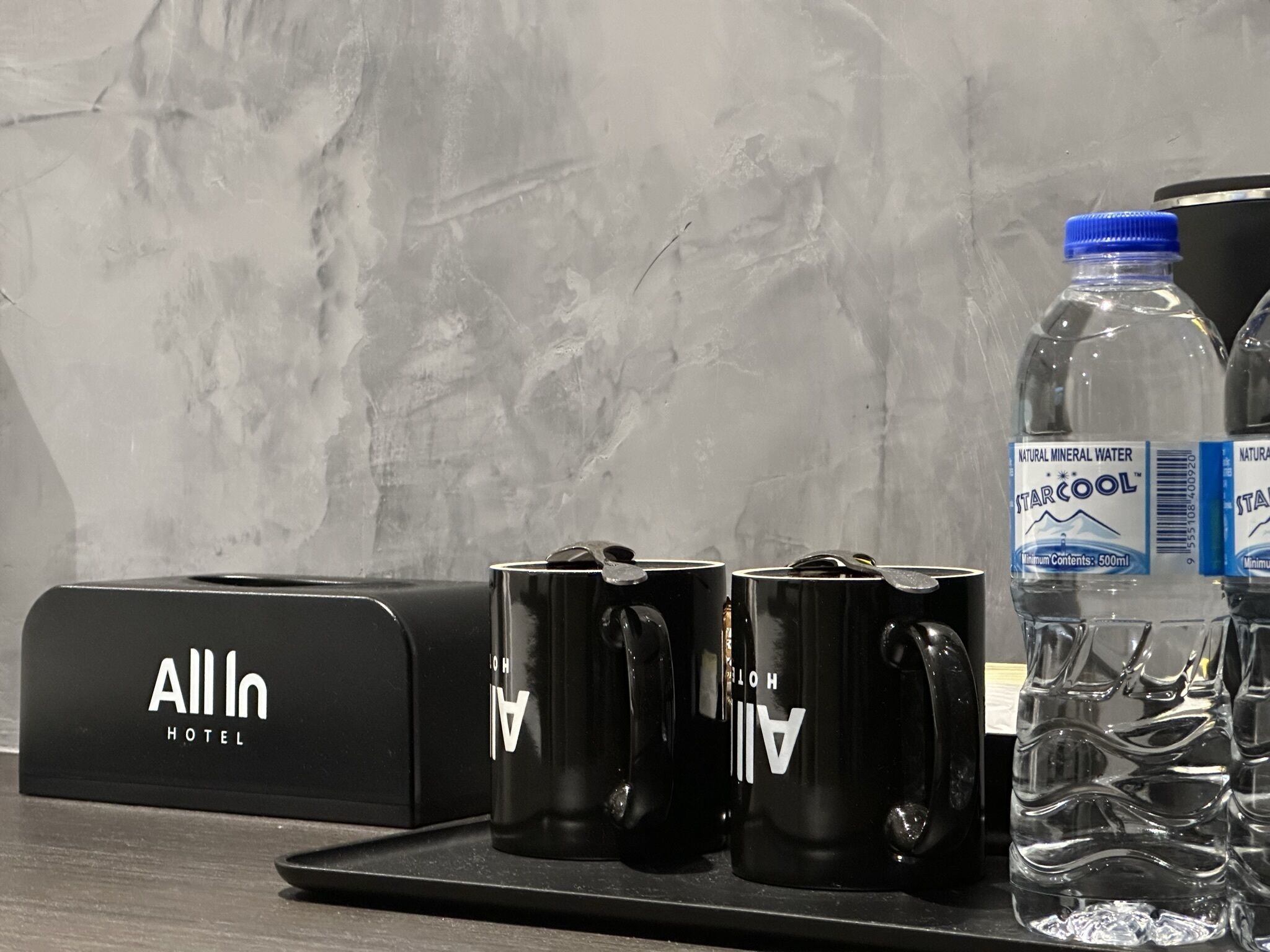 A hotel minibar setup with a water bottle and two black mugs.