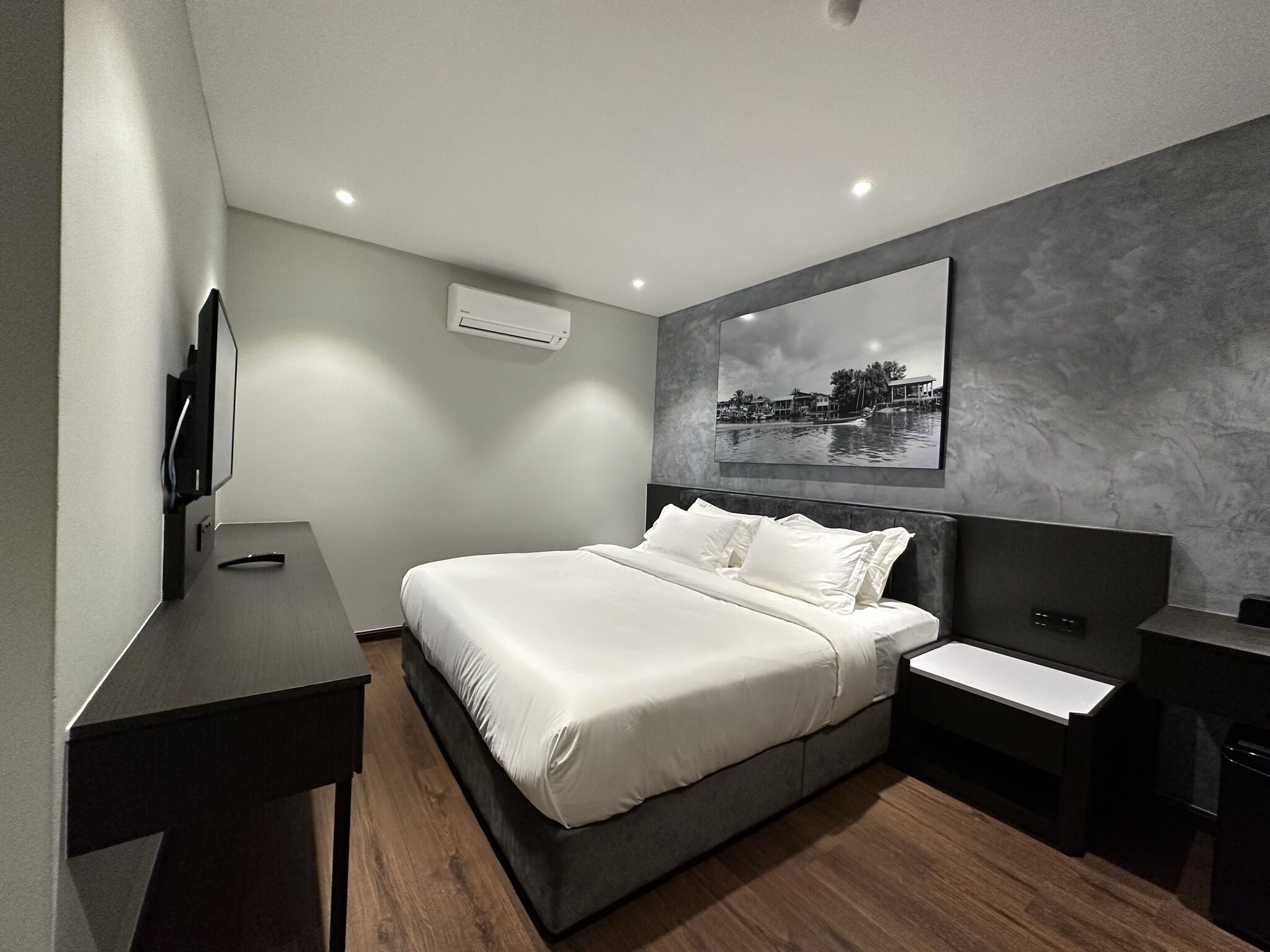 A modern hotel room with a large bed, bedside tables, a flat-screen TV, and a wall-mounted air conditioner.