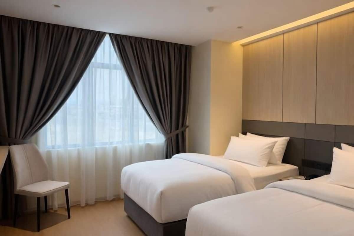 A hotel room with two beds, a chair, and a large window with curtains.