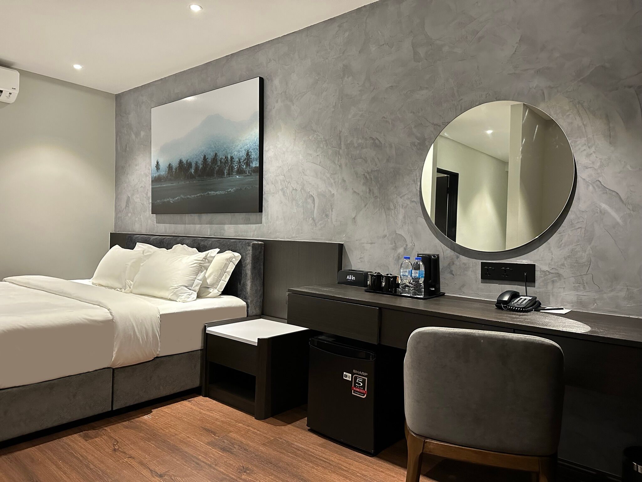 A modern bedroom with a bed, a desk, a chair, a mirror, and a painting on the wall.