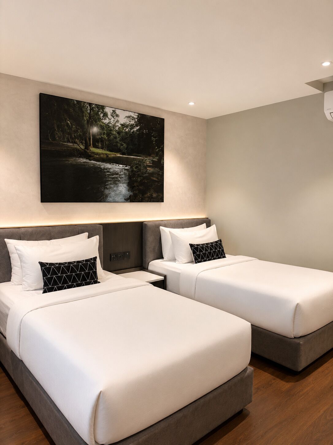 A hotel room with two beds, a nightstand, a wall-mounted painting, and a ceiling light.