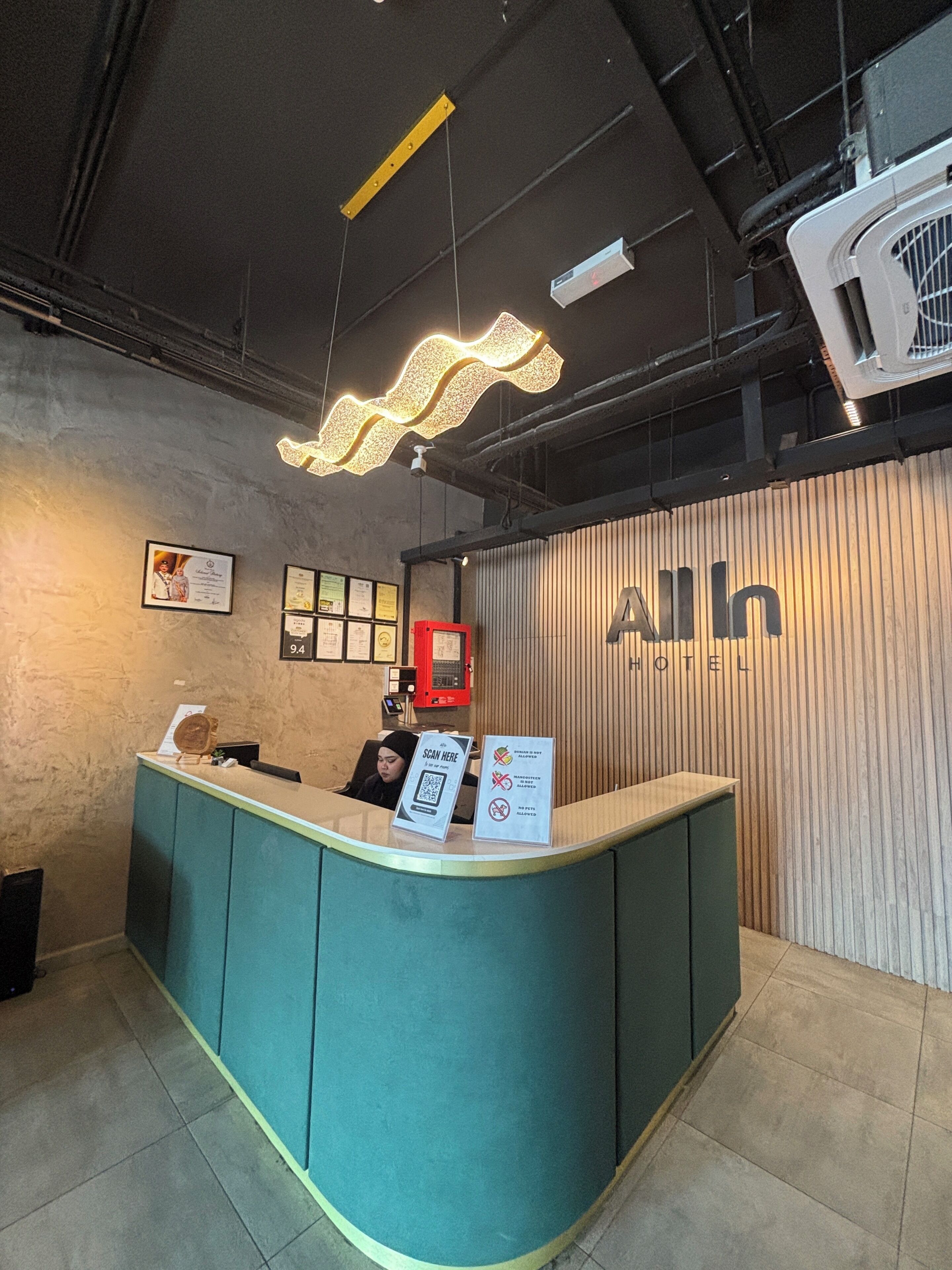A reception desk with a digital screen, a red emergency phone, and framed certificates on the wall.