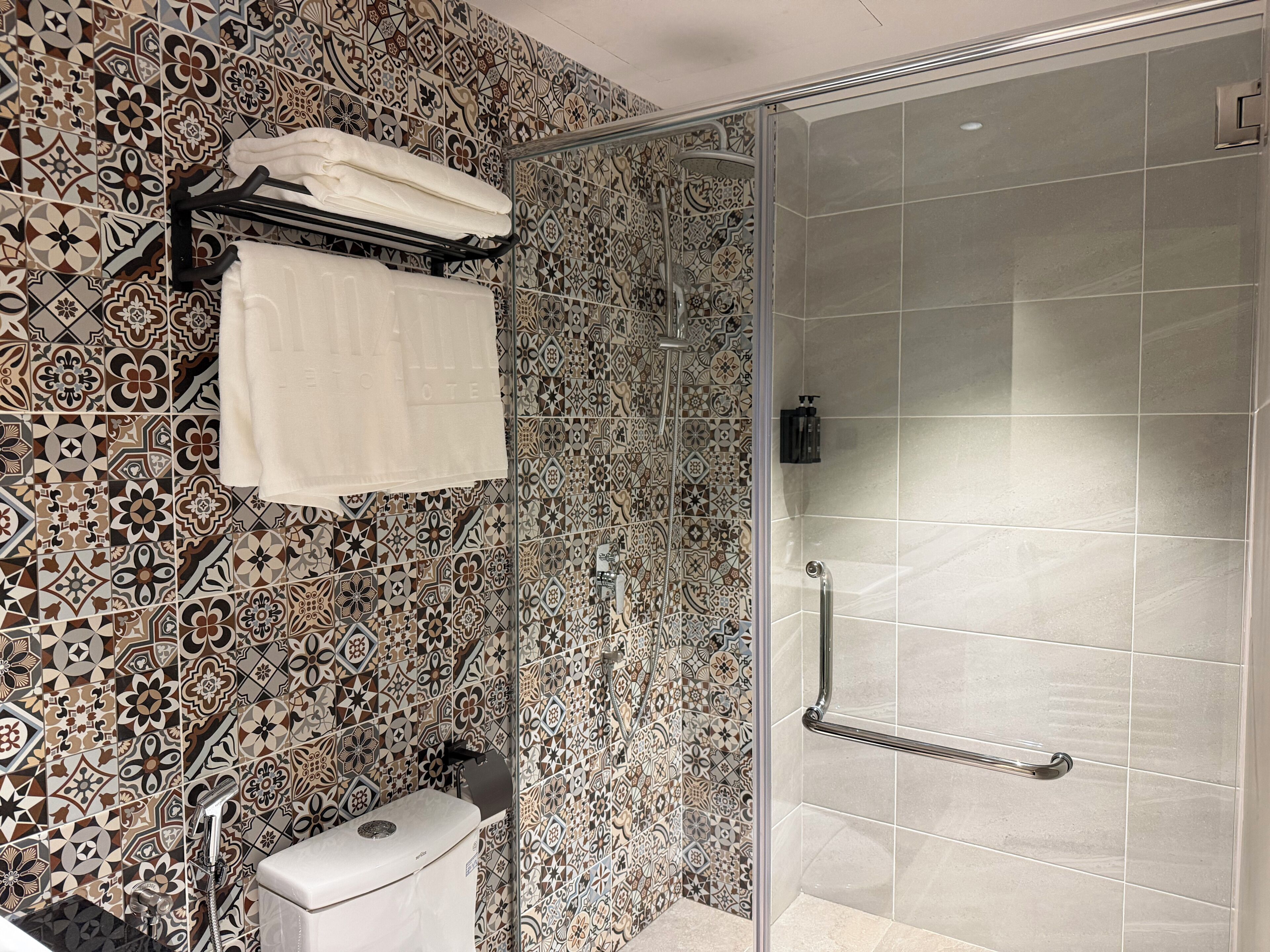 A bathroom with patterned tiles, a glass shower enclosure, a toilet, and a towel rack.
