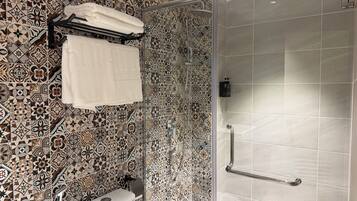 Un baño con baldosas estampadas, cabina de ducha de vidrio, inodoro y perchero.