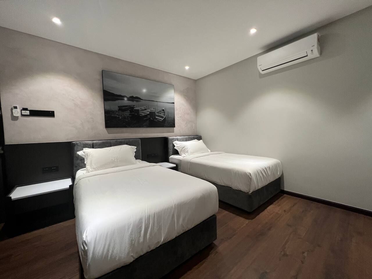 Una camera d'hotel moderna con due letti, un'opera d'arte appesa al muro, un condizionatore d'aria e un comodino con un telefono.