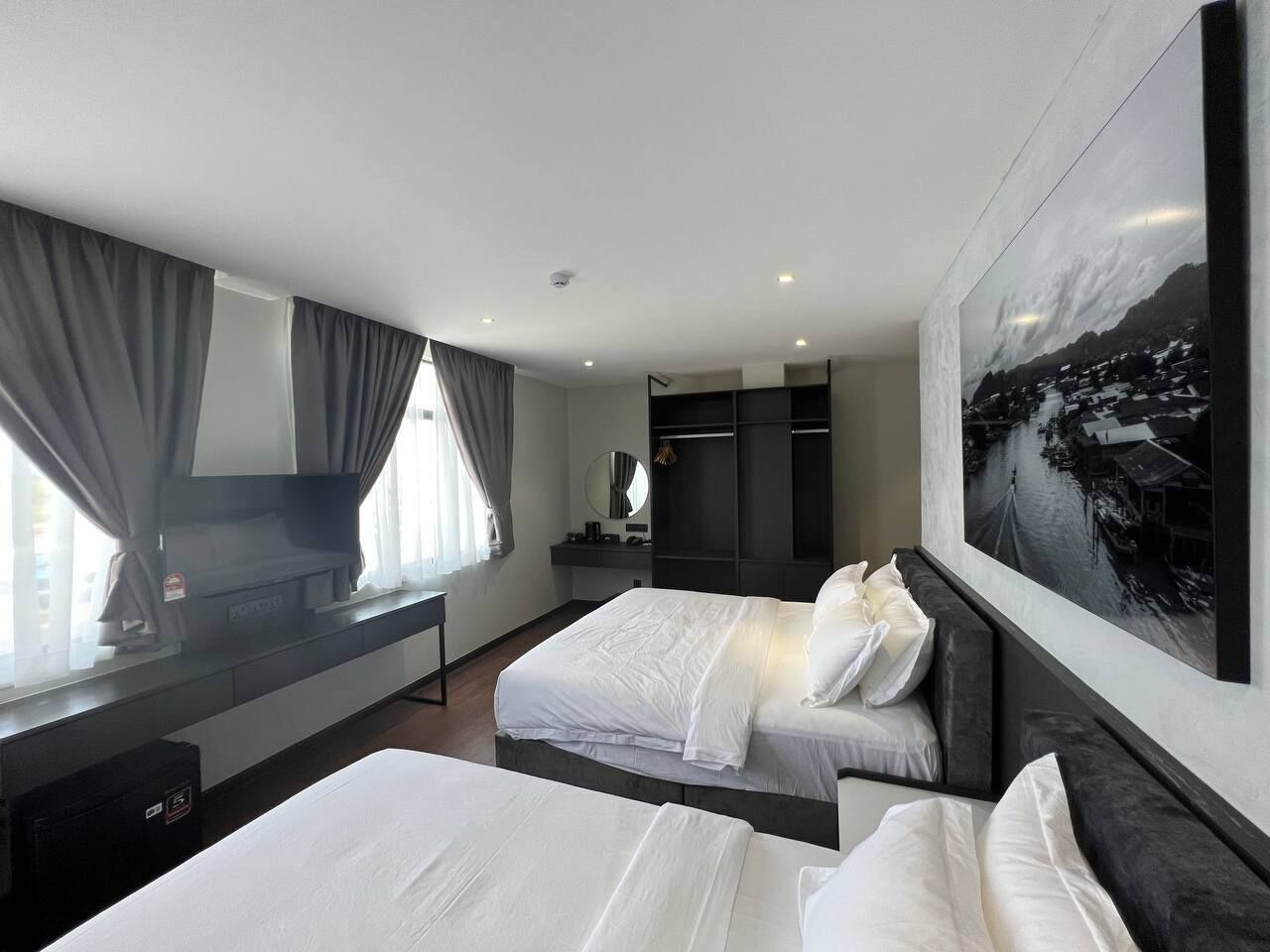 Una habitación de hotel moderna con dos camas, un ventanal con cortinas, un televisor de pantalla plana, un armario y un cuadro grande en la pared.