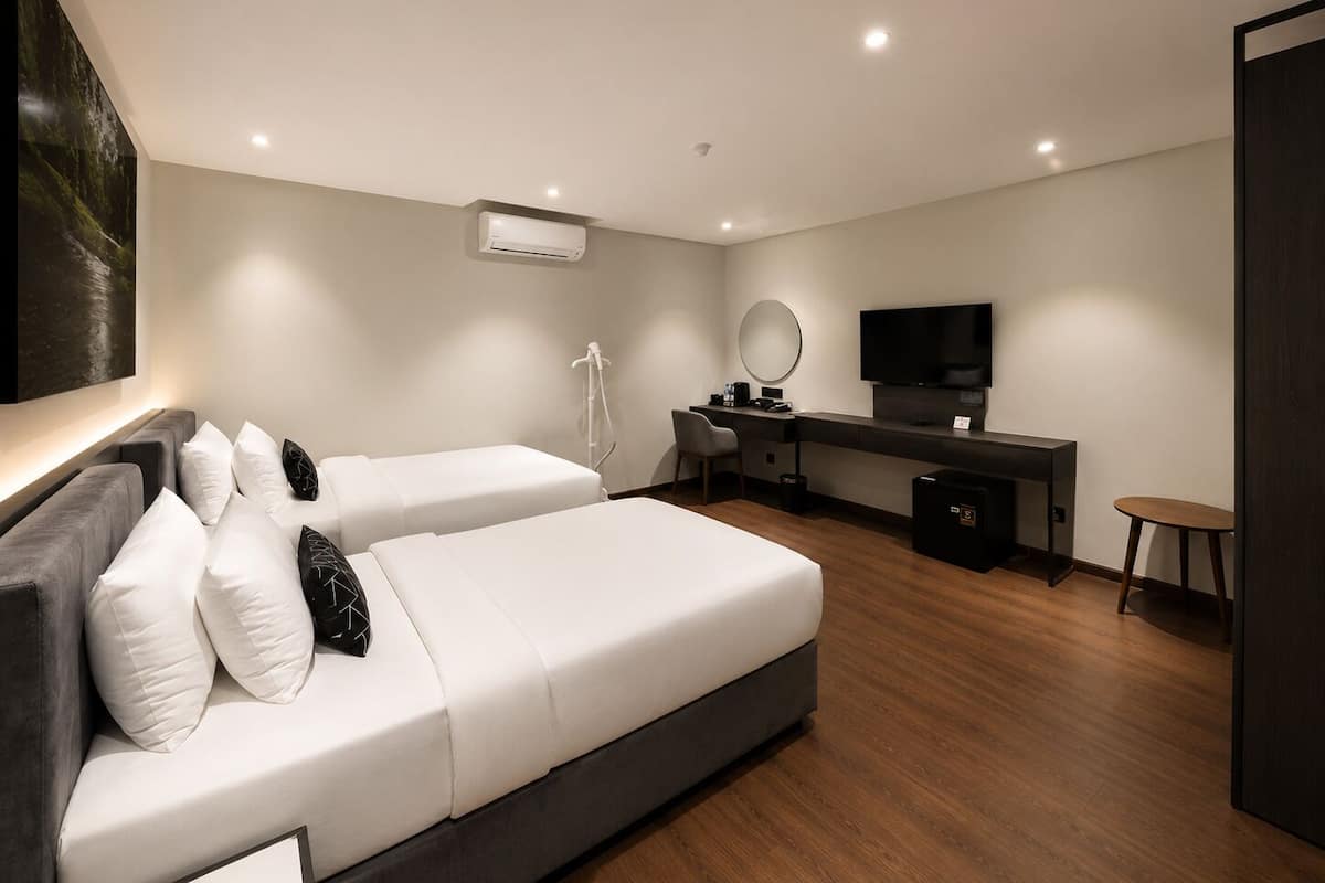 A modern hotel room with a large bed, a desk with a computer, a TV, and an air conditioning unit.