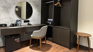 Un baño moderno con pared de mármol, un espejo redondo, un tocador negro, una silla gris, una pequeña mesa de madera y un cubo de basura negro.