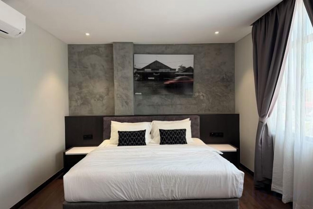 A modern hotel room with a large bed, a headboard with a built-in TV, and a painting on the wall.