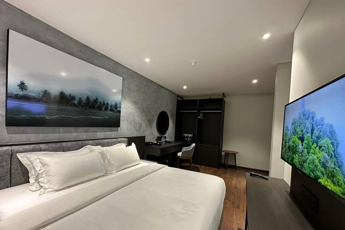A modern hotel room with a large bed, a desk, a chair, and a TV.