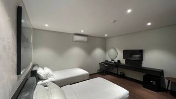 A modern hotel room with two single beds, a desk with a chair, a flat-screen TV, and a small table.