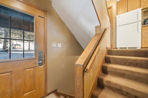 A wooden door with a window, a staircase with wooden railings, and a white refrigerator in a kitchen area.