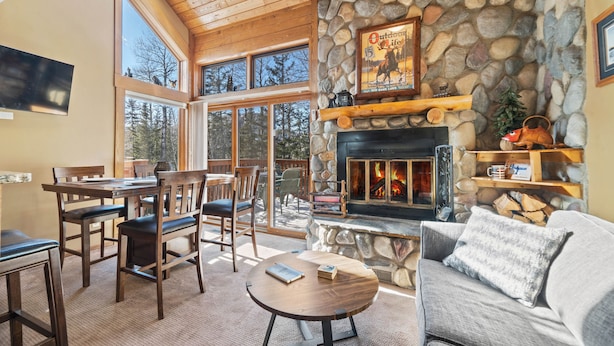 Un interior acogedor con chimenea de piedra, muebles de madera y ventanas amplias que ofrecen vistas al exterior.