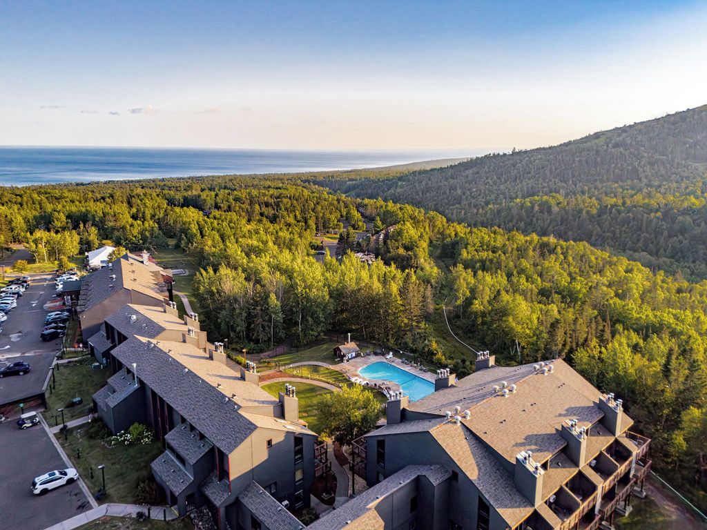 A resort with multiple buildings, a swimming pool, and a forested backdrop.