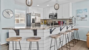 A kitchen with white cabinets, stainless steel appliances, a marble countertop, and bar stools. - Family Tides: Waves, Sun and PrimeTime fun for EvERYONE! (Carolina Beach)