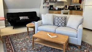 Un espacio habitable compacto con sofá, mesa de centro y una zona de cocina con armarios y electrodomésticos.