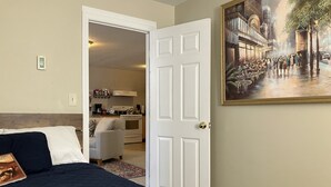 Un dormitorio con una cama, una puerta que da a una cocina y un cuadro en la pared.