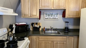 Una cocina con armarios de madera, microondas, estufa, fregadero y licuadora.