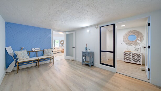 A spacious room with a wooden floor, a blue accent wall, a wooden bench with cushions, a small side table, and a large mirror on a white cabinet. - Welcome to your Dream Villa in the Florida Keys! (Key Largo)
