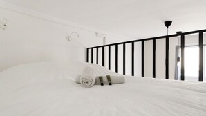 A minimalist bedroom with a large bed, a black railing, and a door leading to a bright room. - Studio Vivienne - Welkeys (Paris)