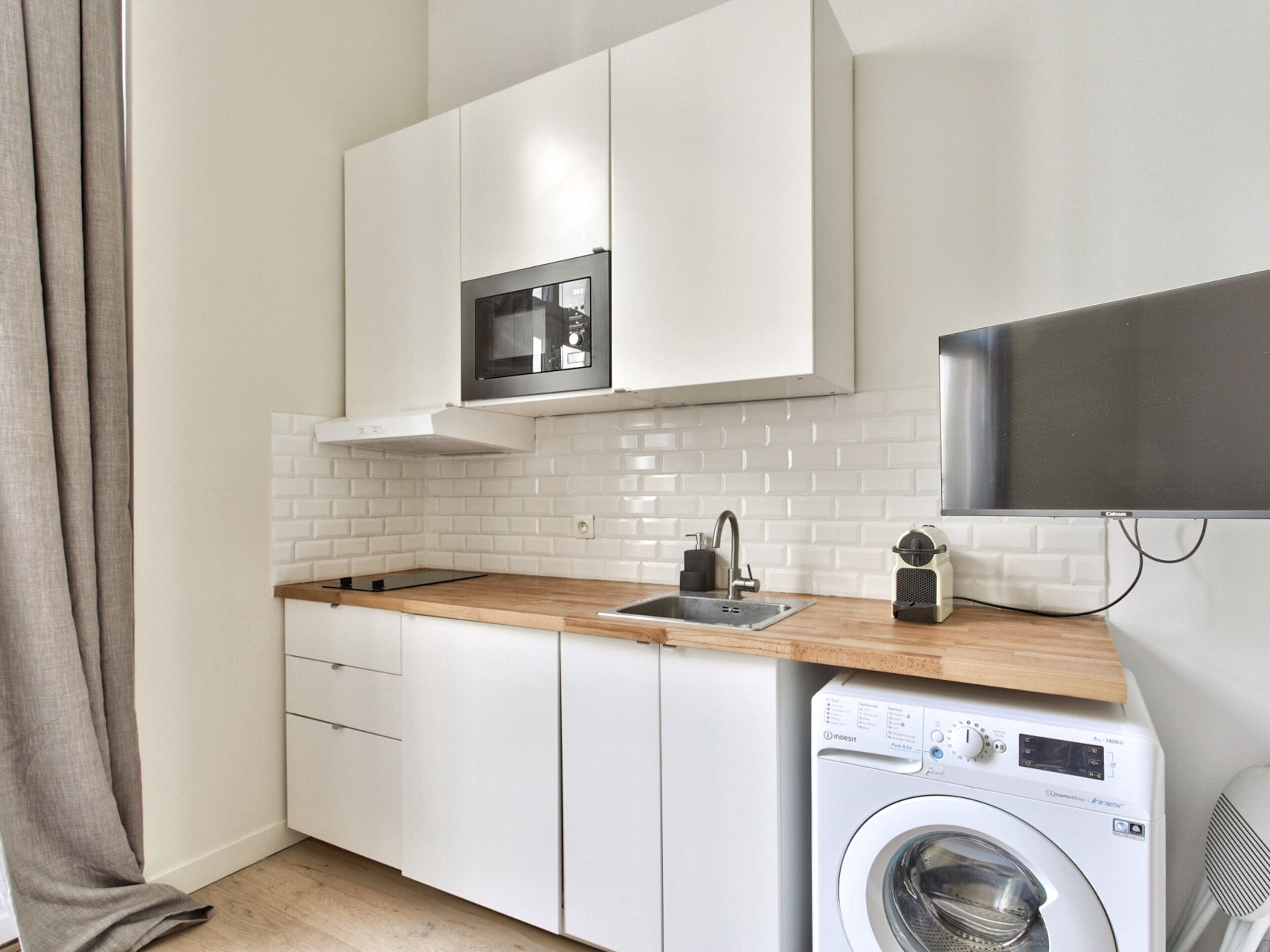A compact kitchen with a built-in microwave, a sink, and a washing machine.