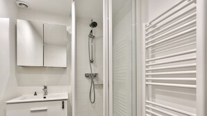 A modern bathroom with a white vanity, a shower with a handheld showerhead, and a towel rack. - Studio Vivienne - Welkeys (Paris)