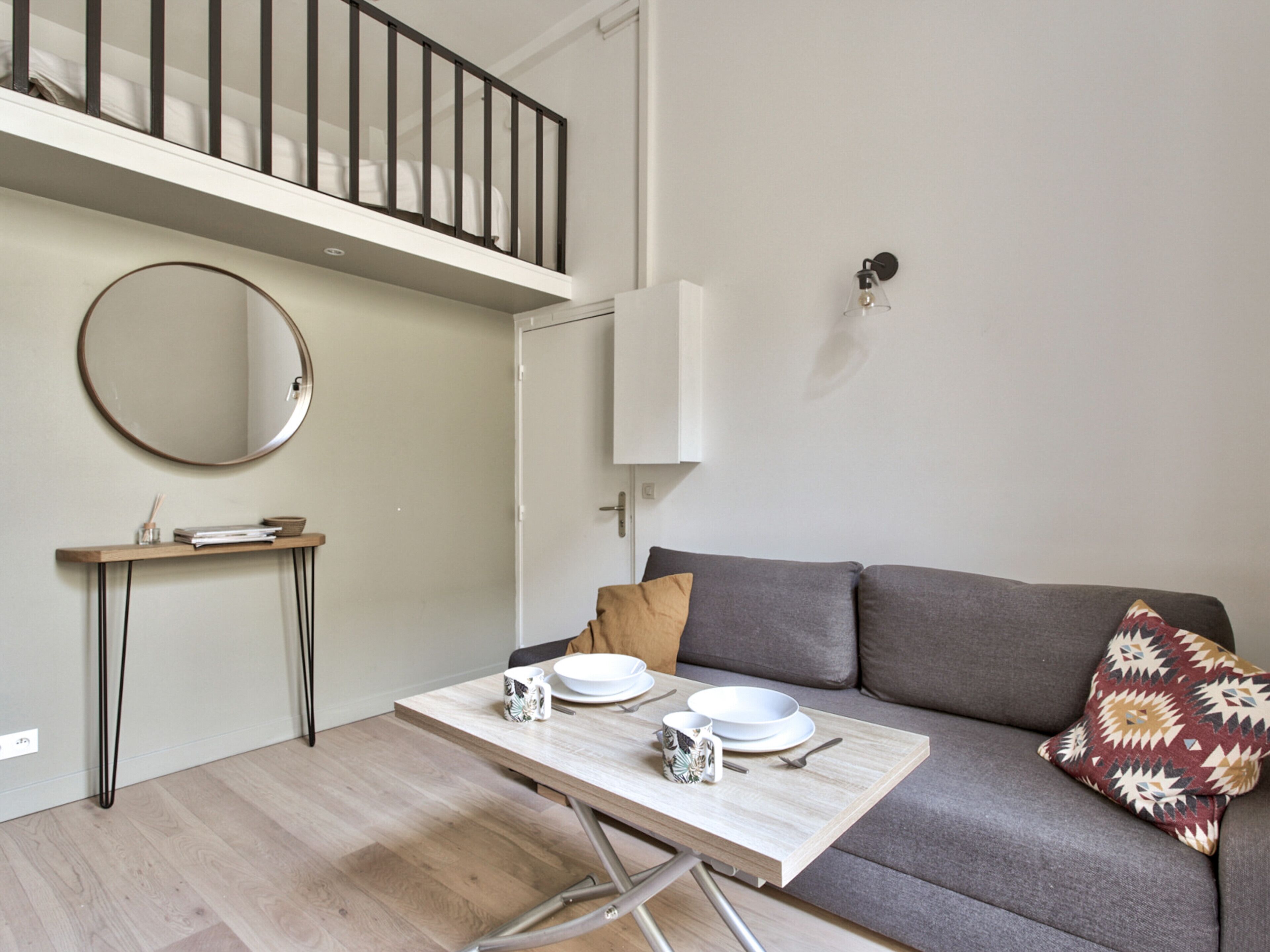 A modern living room with a grey sofa, a wooden coffee table, and a round mirror on the wall.