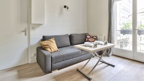 A modern living room with a grey sofa, a small table with a white tablecloth, and a window with a view of buildings. - Studio Vivienne - Welkeys (Paris)