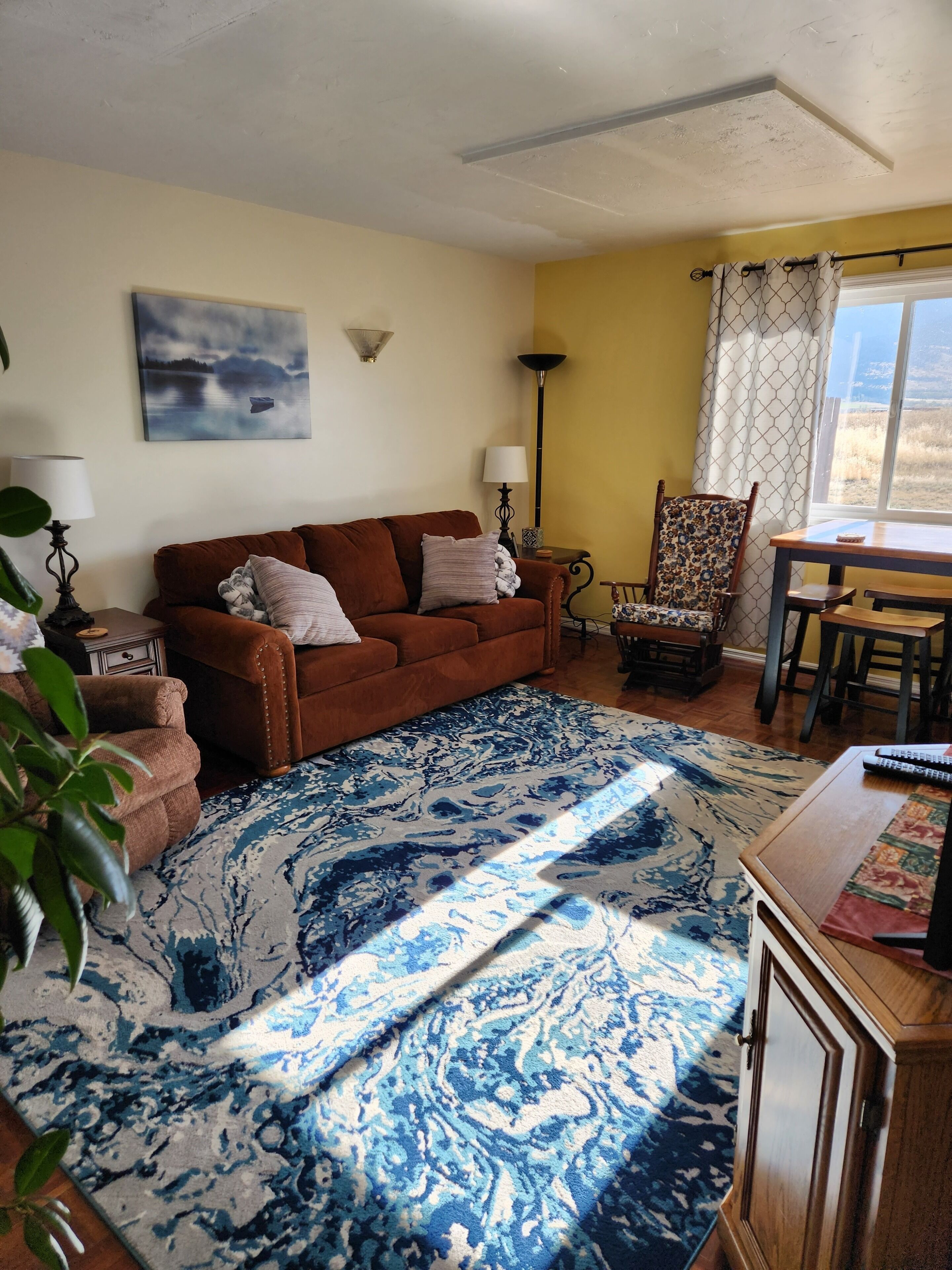 A living room with a brown sofa, patterned rug, and a dining area with a table and chairs.