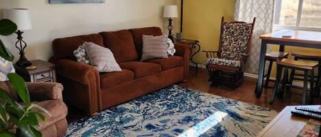 A living room with a brown sofa, patterned rug, and a dining area with a table and chairs.
