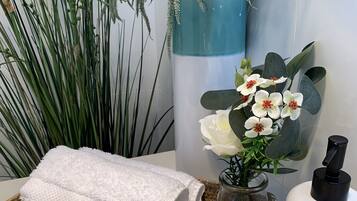 A bathroom with a white towel, a bottle of shampoo, a bottle of conditioner, and a bottle of lotion on a woven tray.