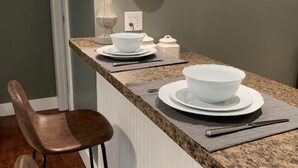Eine Küche mit einer Granitarbeitsplatte, zwei braunen Stühlen, einer weißen Schüssel auf einem Teller, einer Uhr, einer Lampe und einer Steckdose.