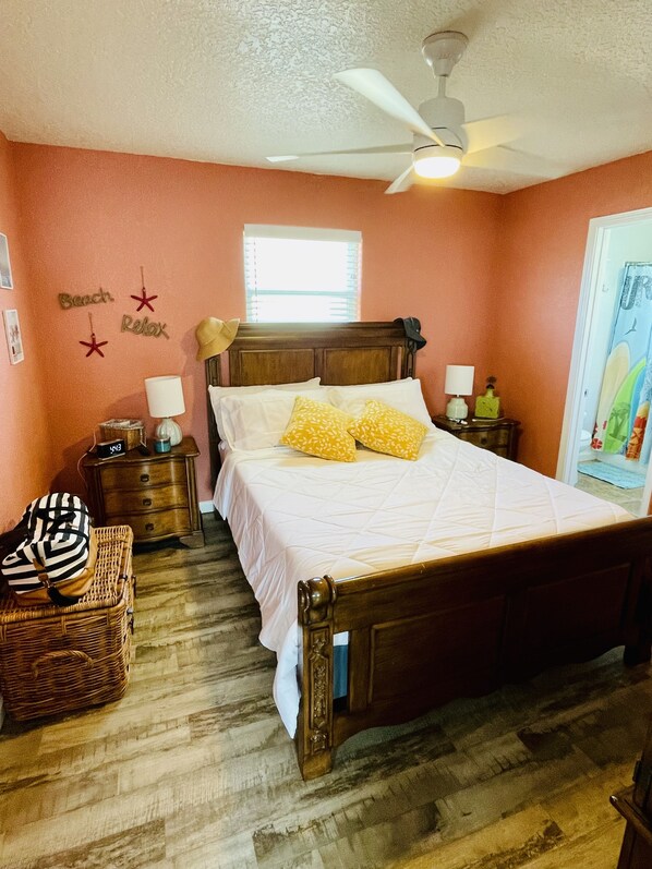 A bedroom with a wooden bed, a nightstand with a lamp, a wicker chair, and a wall with decorative stars and the words "Beach Relax".