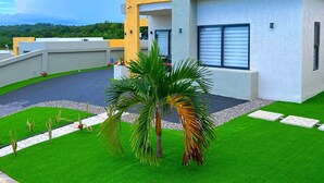 A modern building with a flat roof, a paved driveway, and a well-maintained lawn with palm trees. - Pyramid Bliss - One Bedroom (Ocho Rios)